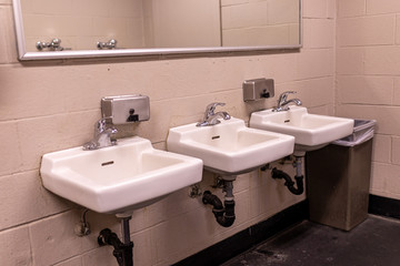 View at three white sink in a men's restroom with metal soap boxes above
