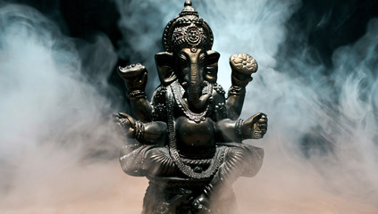 Hindu god Ganesha on black background. Statue with a smoke of incense.  - obrazy, fototapety, plakaty