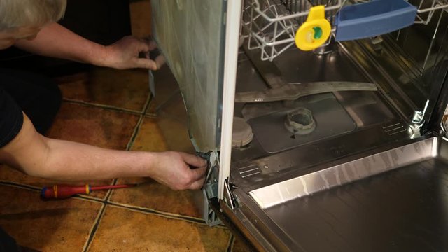 Handyman fixing broken dishwasher machine with a screwdriver.