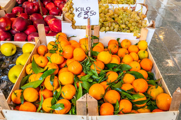 Oranges/ tangerine with stems and leaves, green grapes red and yellow apple fruits on display at local farmers market. Fresh ripe raw organic colorful fruit on sale at marketplace store.