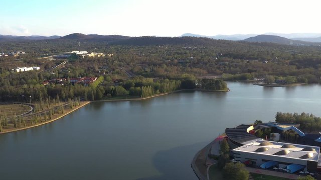 Aerial view of Canberra City, Australia, travelling over Lake Burley Griffin and Acton Peninsula toward Australian Parliament House on a sunny afternoon 