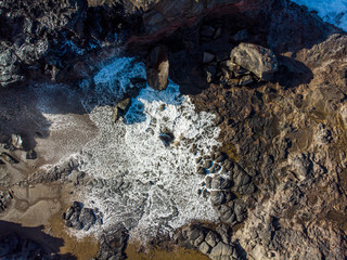 Aerial view from above at a Nakalele blowhole after water eruption, Maui, Hawaii. White sea foam and water spray on a rocks around a hole in the ground