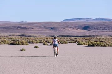 Foto op Canvas A teen age girl  riding a bike on a playa of Alvord lake against Steens mountains in the background © Dmitry