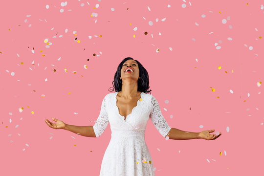 Portrait of a happy young woman in white dress and black hair smiling and looking up while celebrating wonderful life with arms out with confetti falling