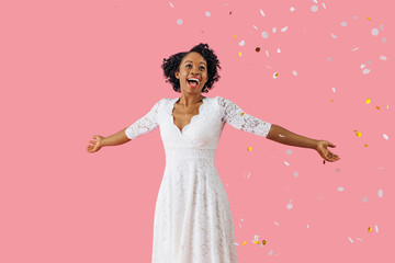 Obraz na płótnie Canvas Portrait of an excited young woman in white dress and black hair smiling with arms out and confetti falling