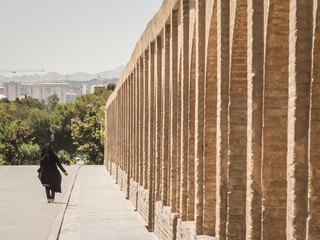 Shape of a woman wearing islamic clothing (niqab and veil) passing by on the Si o Seh Pol bridge on the afternoon in Isfahan, Iran. Also known as Allahverdi Khan Bridge, it is a major landmark