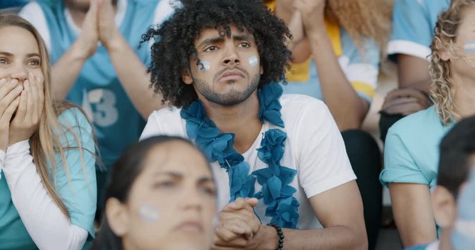 Man looking nervous while watching soccer match in stadium. Group of anxious looking Argentinian football fans in stadium.