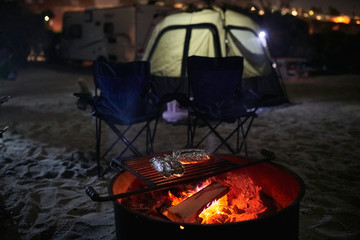 Cooking Aluminum Foil Wrapped Food on a Camp Fire Ring Grill with Tent in the Background