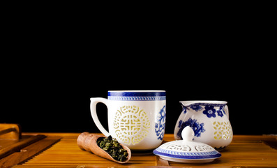 Chinese tea ceremony. Ceramic tea cup and jug with green oolong tea Tieguanyin and scoop on a bamboo desk, black background. 
