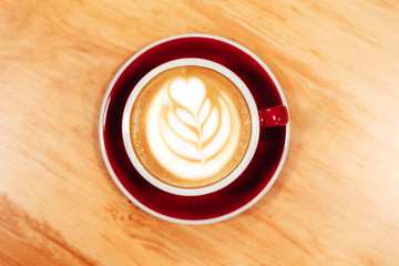 Cappuccino with frothy foam, red coffee cup top view closeup on wooden background. Flat lay style.