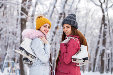 Fototapeta premium Happy beautiful brunette women with ice skates go to the rink, winter outdoors