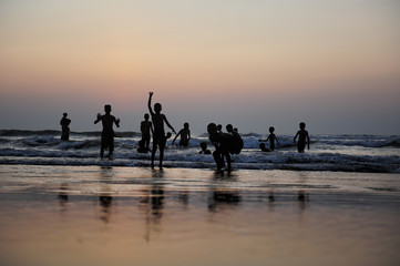 Fototapeta premium Silhouettes of children jumping in the surf on the background of the sea and evening sky. Boyish figures, children playing on seashore. Carefree childhood, concepts of freedom and the future.