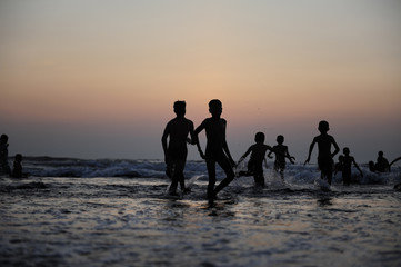 Silhouettes of children jumping in the surf on the background of the sea and evening sky. Boyish figures, children playing on seashore. Carefree childhood, concepts of freedom and the future.