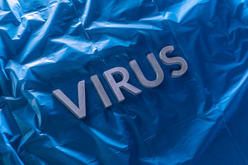 the word virus laid with silver metal letters on crumpled blue plastic film with dramatic light