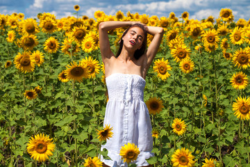 Naklejka na ściany i meble Portrait of a young beautiful girl in a field of sunflowers