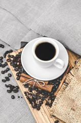 Coffee white cup and saucer on a wooden board with coffee beans and cinnamon on a gray linen tablecloth. Good morning