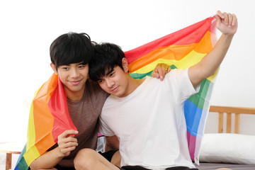 Asian homosexual gay man holding lgbt rainbow flag while sitting at home, Happy asia boys holding homosexsual flag, lgbt symbol sign, Diversity people concept © mangpor2004