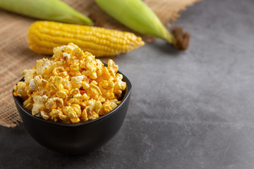 Popcorn in the black bowl and raw corn on the black table. High angle view.