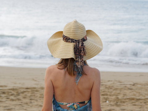Summer holidays, vacation, travel and people concept. Woman in sun hat on beach over ocean and blue sky background. Back view.