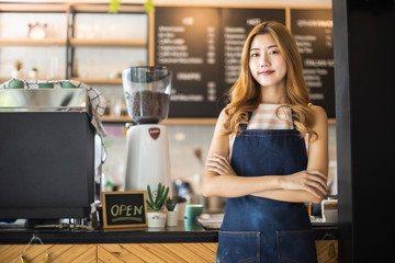 Fototapeta na wymiar Pretty young asian waitress standing arms crossed in cafeteria.Coffee Business owner Concept. barista in apron smiling at camera in coffee shop counter