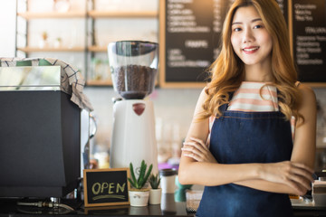 Pretty young asian waitress standing arms crossed in cafeteria.Coffee Business owner Concept.  barista in apron smiling at camera in coffee shop counter