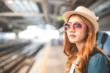 Happy Asian couple traveler holding a mobile phone in station and waiting for train in vacation time. Young Asian Tourists With Backpacks Train travel in Sightseeing City Thailand.