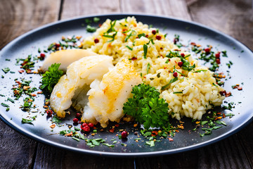 Risotto with fried cod loin on wooden background