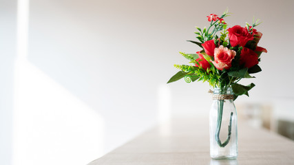 Bouquet of red plastic roses in a glass bottle placed on a wooden table. Wedding decorations,...