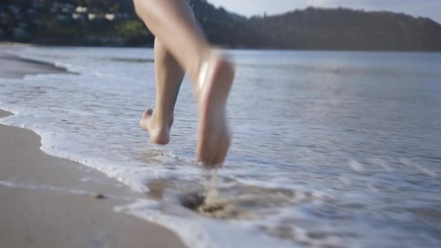 Female legs is running on the sand. Morning run on the sandy seashore. Evening tide. Splashing into the camera. Recreation of young woman closeup. Outdoor sports.