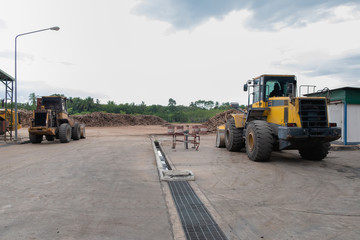 The tractor is in an industrial park. With pieces of wood arranged in a pile