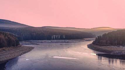 Frozen dam in the winter forest at sunset. A pink illuminated sky above Ecker Reservoir and Ecker Dam near Bad Harzburg, Harz mountain range, Lower Saxony/Saxony-Anhalt, Germany.