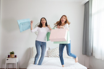 Fototapeta na wymiar Cheerful happy Asian woman enjoying shopping: she is carrying shopping bags and jump ob bed.Happiness beautiful two friends jumping .