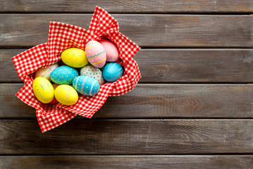 Basket with painted eggs for Easter dinner on dark wooden desk top-down copy space