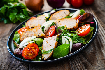Caesar salad - barbecue chicken breast and vegetables on wooden table