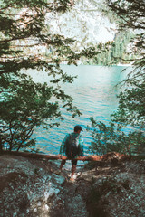 man with backpack sitting at wood log enjoying water view