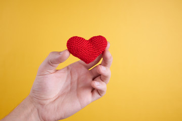 male person hold wool heart in his hand isolated on an yellow background. romance and valentine day concept.