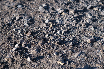 Stones of different sizes lie on a dusty surface. Dirt road in the sun.