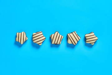 Row of striped white and dark chocolate candies in shape of star lies on blue countertop. Top view. Close-up