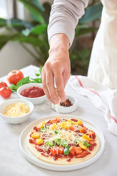 Baker's hand placing ingredients on pizza