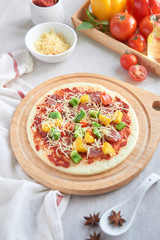 Raw pizza with ingredients in the background