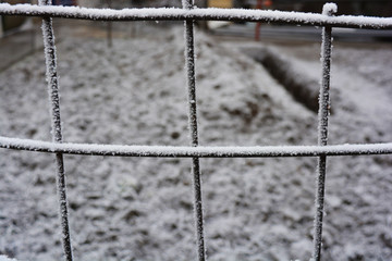 A metallic old rusty square-headed, square mesh, a cage decorated with white snow, bright hoarfrost and beautiful snowflakes.