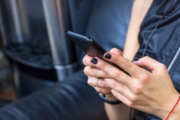 A girl in leather clothes with black nails sits on a leather sofa and holds a phone in her hands. Selective focus