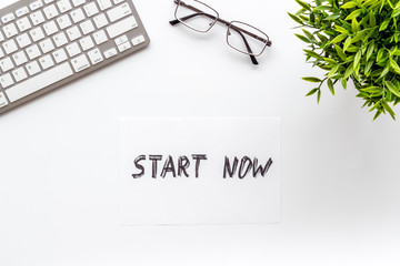 Start now. Motivative text on white office desk top-down