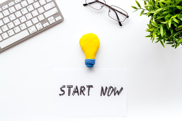 Start now. Motivative text on white office desk top-down