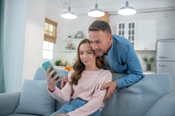 Dad with daughter looking at smartphone screen happy.