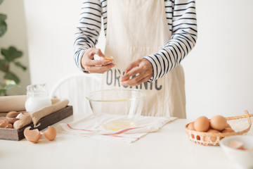 Male hands are breaking an egg into bowl to make dough on white table