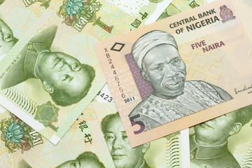 A close up image of a peach colored, five Nigerian naira bank note on a background of Chinese one yuan bank notes