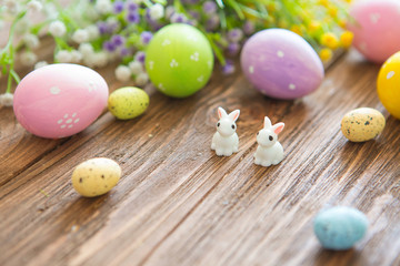 Obraz na płótnie Canvas Happy Easter concept. Easter eggs with flowers and small bunny toys on wooden board, easter holiday concept.