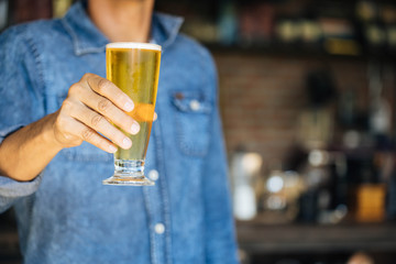 A man wearing a denim shirt and a glass of beer in the bar	