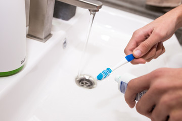 Toothbrush with toothpaste in the guy's hand on the background of the washbasin.
